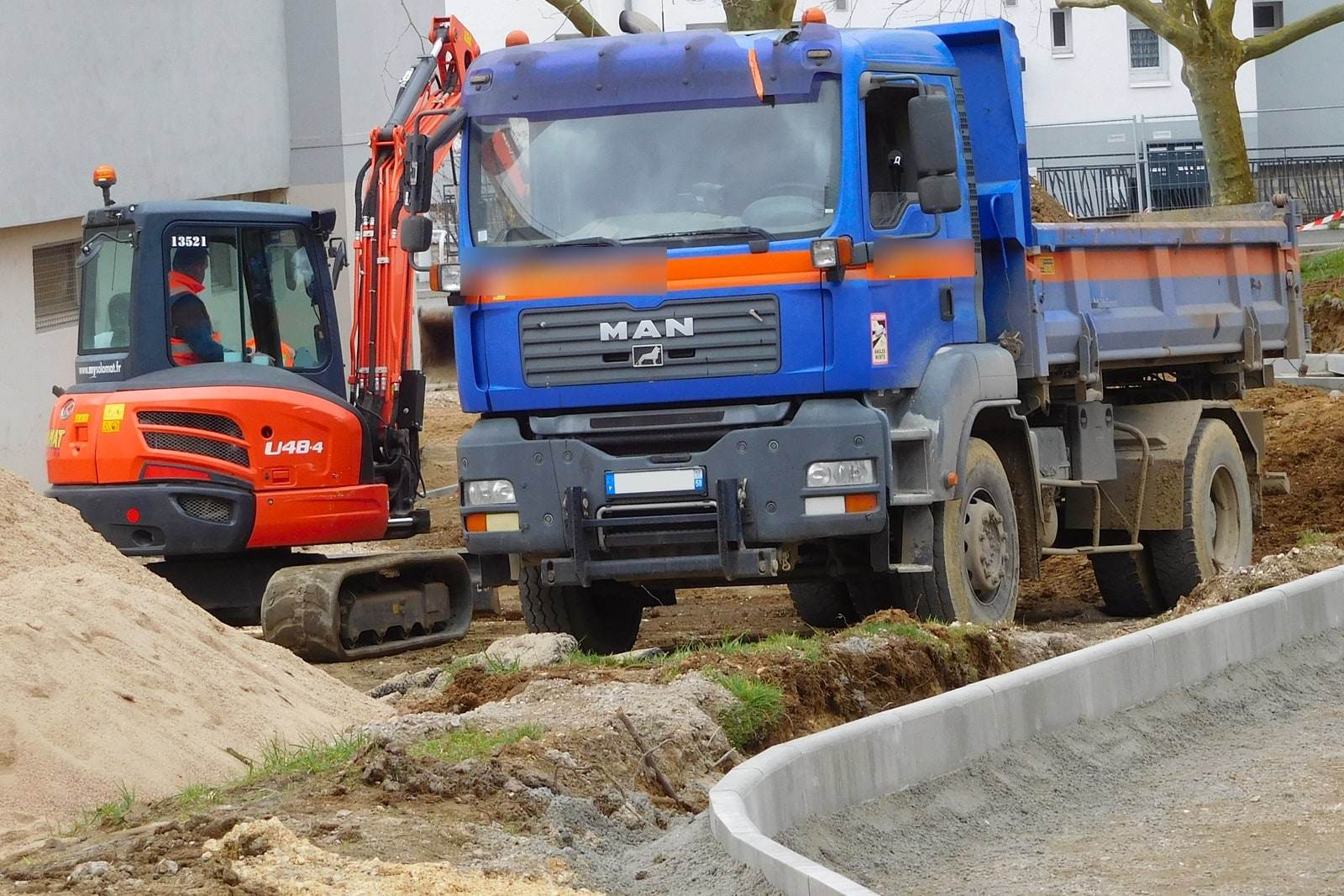 Un camion benne et une mini-pelle sur un chantier de terrassement, à côté d'un tas de terre de remblai.